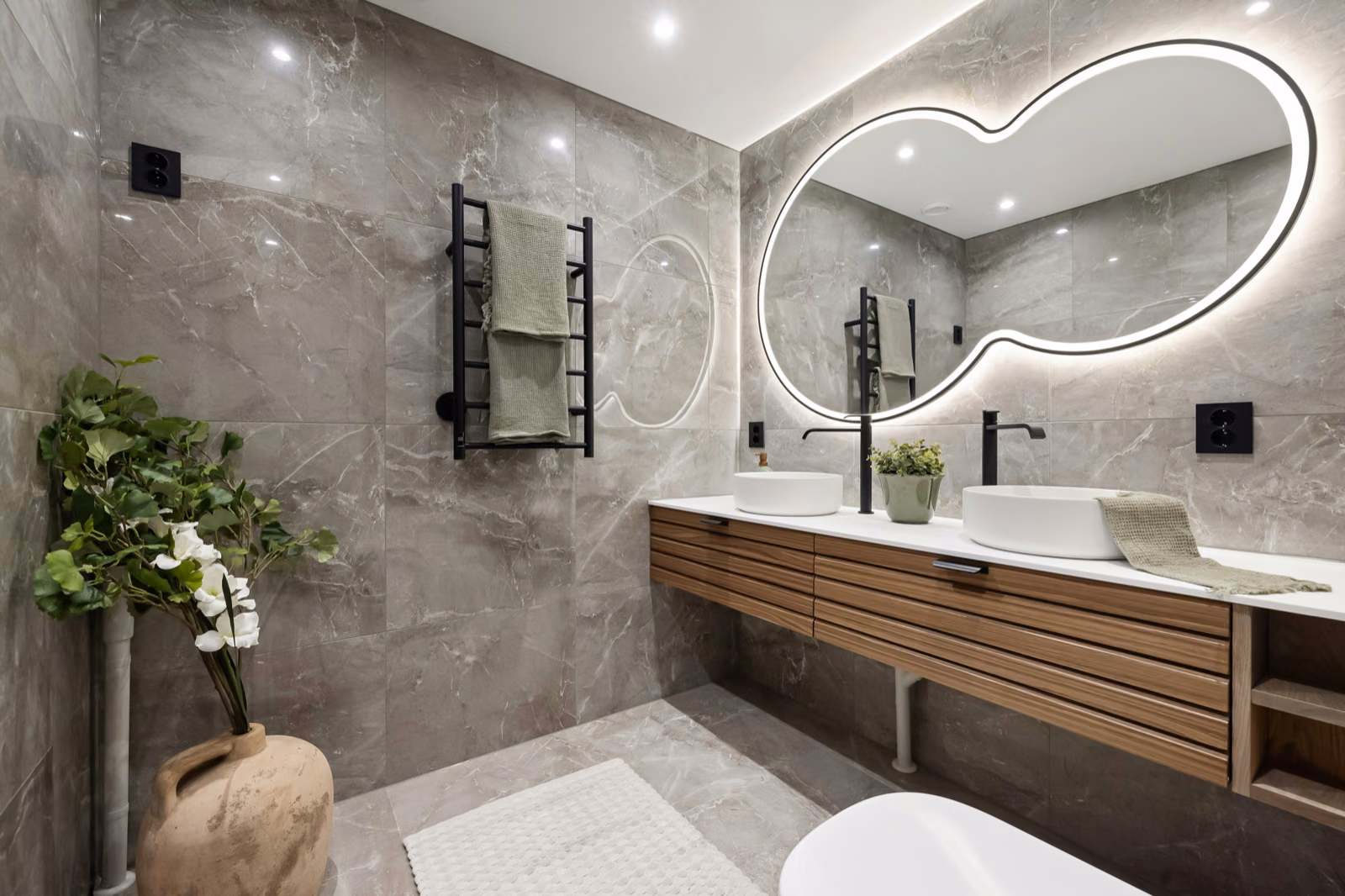 A modern and airy bathroom interior with a focus on the sink and vanity area. The Renotive vanity is made of sleek, white marble with clean lines and minimalist hardware. Soft, natural lighting filters in through large windows, creating a serene and relaxing ambiance. The backsplash features elegant, neutral-toned tiles that complement the vanity. Subtle potted plants add a touch of greenery, while a large mirror above the vanity reflects the space, creating a sense of openness. The overall aesthetic is sophisticated, inviting, and reflective of the "Assessing Your Bathroom Remodel Needs" section of the article.
